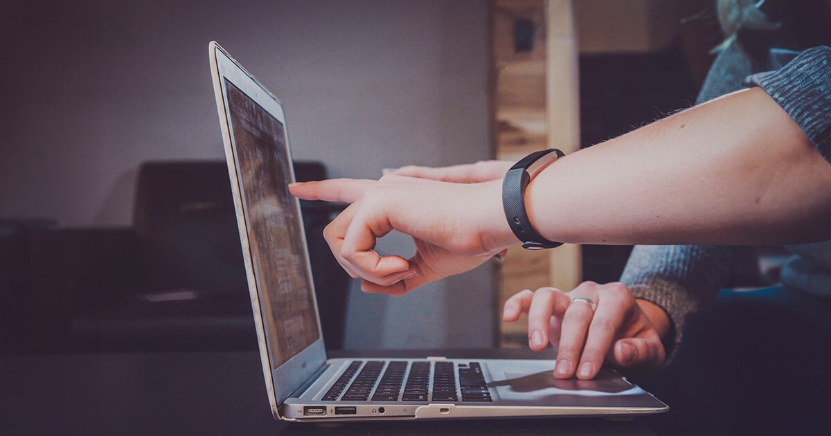 Two people working at a laptop with the screen showing code.